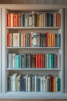 Vintage hardcover books arranged on white wooden built-in bookshelf, featuring harmonious color palette of red, blue, and neutral tones. Classic library interior.