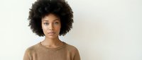 Young African American woman with natural curly afro hair wearing brown sweater against neutral background for lifestyle and fashion content.