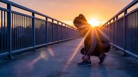 Silhouetted figure crouching on pedestrian bridge at sunrise, golden sunlight creating dramatic lens flare effect. Suitable for motivational, wellness, and lifestyle content.