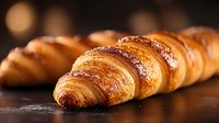 Fresh baked golden croissants with flaky layers and sesame seeds on dark background, close up view showing buttery texture and crispy crust.