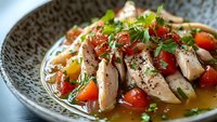 Grilled chicken breast with cherry tomatoes and fresh herbs in savory broth, served in decorative ceramic bowl. Healthy Mediterranean cuisine.