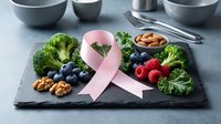 Pink ribbon with healthy foods broccoli blueberries strawberries walnuts on slate board cancer awareness nutrition prevention concept.