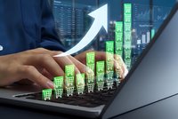 Online shopping growth concept with businessman hands typing on laptop and green shopping cart icons rising upward with white arrow on digital background.