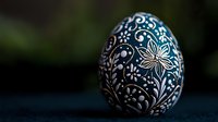 Decorative Easter egg with intricate white floral folk art pattern hand-painted on dark blue background, traditional Slavic design photographed with soft focus.