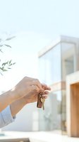 Hand holding house keys with wooden keychain in bright modern home interior for real estate and property ownership concept.