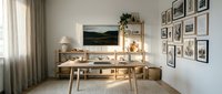Scandinavian home office with wooden desk, gallery wall frames, potted plant, desk lamp, and natural light from window with curtains.
