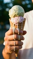 Hand holding double scoop ice cream cone with pistachio and strawberry flavors melting in summer sunlight, perfect for food and beverage marketing.