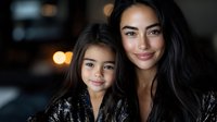 Young Asian mother and daughter with long dark hair and radiant smiles wearing black lace dresses pose together in intimate portrait with soft bokeh lighting.