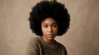 Young African American woman with natural afro hairstyle wearing knitted sweater against neutral background for lifestyle and fashion content.