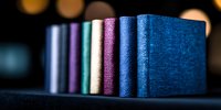 Row of colorful hardcover books standing on dark shelf with blurred bokeh background, selective focus on blue and purple spines creating artistic composition.