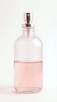 Transparent glass spray bottle filled with pink liquid fragrance, featuring rose gold metallic pump dispenser on white background, ready for cosmetics and perfume packaging design.