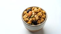 Homemade granola with nuts and dried fruits in ceramic bowl on white background. Healthy breakfast cereal mix for morning meal and snacking.