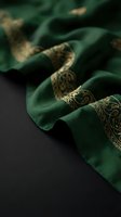 Elegant emerald green silk fabric with ornate golden paisley embroidery flowing gracefully on dark surface for luxury fashion and textile design projects.