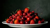Fresh red strawberries, cherries, and raspberries piled on a white plate against a dark background, showcasing vibrant summer fruits.