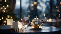 Golden teapot and cup on wooden table with blurred Christmas tree and bokeh lights creating cozy winter atmosphere. Festive holiday tea time setting.