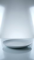 Empty white ceramic plate on reflective surface with studio lighting, suitable for food photography, product mockups, and culinary design projects.