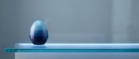Blue gradient egg-shaped object on transparent glass surface with soft lighting and minimalist composition for modern design projects.