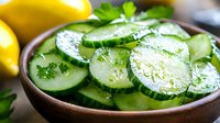 Fresh sliced cucumber salad with herbs in wooden bowl, bright yellow lemons in background, healthy vegetarian appetizer for summer menu.