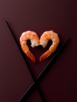 Fresh cooked shrimp arranged in heart shape with black chopsticks on dark burgundy background, creative food photography for restaurant menu or Valentine's day concept.