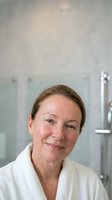 Middle-aged Caucasian woman in white medical coat smiling confidently in modern healthcare facility with professional equipment background for medical content.