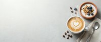 Overhead view of two cups with latte art and granola bowl surrounded by coffee beans and spoons on light surface for café and breakfast content.