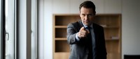 Professional businessman in dark suit pointing finger at camera in modern office interior with wooden shelving and natural lighting for corporate presentations.