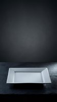 Empty white rectangular plate on dark textured surface against moody charcoal backdrop, suitable for food photography, restaurant menus, culinary presentations, and dining concepts.
