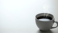 Steaming hot black coffee in gray ceramic mug on white surface with copy space for morning beverage and cafe concepts.