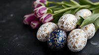 Decorated Easter eggs with golden snowflake patterns and fresh pink tulips on dark background. Traditional holiday celebration composition.