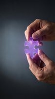 Hands holding glowing purple puzzle piece symbolizing solution finding and problem solving in business strategy and teamwork concepts.