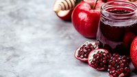 Fresh pomegranate seeds, red apples and homemade berry jam on gray concrete background. Natural healthy ingredients for seasonal cooking and preserves.