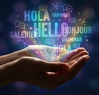 Hand holding glowing neon text displaying hello in multiple languages with grammar icons and floating particles on dark blue background for language learning and education.