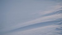 Pristine snow drifts create flowing patterns across winter landscape with soft blue shadows and gentle curves formed by wind erosion.