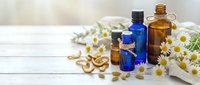 Essential oils in amber and blue glass bottles with fresh chamomile flowers and herbs on white wooden background for natural wellness and aromatherapy.