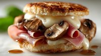 Gourmet sandwich with melted cheese, sliced mushrooms and ham on artisan bread roll. Delicious comfort food for restaurant menu or cooking blog content.