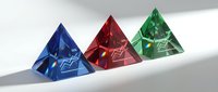 Three colorful crystal pyramids in blue, red and green arranged in row casting shadows on white surface for luxury jewelry design and gemstone concepts.