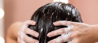 Young woman applying hair mask treatment to wet dark hair in bathroom for healthy haircare routine and scalp nourishment.