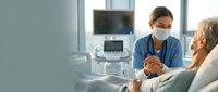Female healthcare professional wearing surgical mask and stethoscope consults with senior female patient in modern medical clinic, discussing treatment options and providing compassionate care.