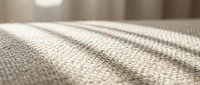 Close-up macro view of natural beige linen fabric texture with soft lighting creating gentle shadows and highlights across woven textile surface.