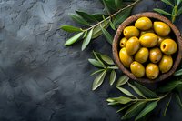 Fresh green olives in wooden bowl with olive tree branches on dark stone background, top view with copy space for Mediterranean cuisine and food design.