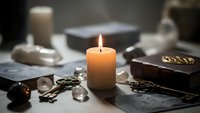 Burning candle surrounded by mystical objects including crystals, old books, and ornamental keys creating atmospheric spiritual workspace for meditation practices.
