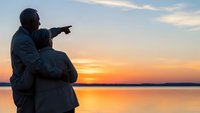 Father and son silhouette pointing at sunset over calm lake water during golden hour family bonding moment with peaceful sky reflection.