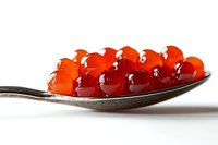 Fresh red caviar on silver spoon against white background, macro shot showing translucent salmon roe pearls with natural glossy texture and rich color.