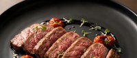 Grilled beef steak sliced and served on black plate with cherry tomatoes and fresh herbs for gourmet dining and culinary presentations.