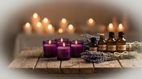 Spa aromatherapy setup with purple candles, essential oil bottles, dried lavender and warm ambient lighting on rustic wooden surface for relaxation.