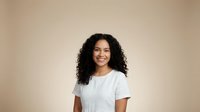 Happy young mixed-race woman with curly hair smiling in white t-shirt against beige background for lifestyle and portrait photography projects.