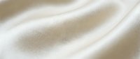 Soft cream colored fabric with gentle folds and smooth texture creating elegant waves and shadows for luxury textile backgrounds and fashion design projects.
