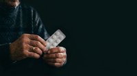 Senior man with weathered hands holding blister pack of medication tablets against dark background, depicting healthcare, aging, pharmaceutical treatment, and medical wellness.