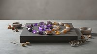 Purple amethyst crystals and healing stones arranged on wooden tray with dried flowers for meditation and spiritual wellness practices.
