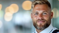 Confident mature Caucasian businessman with beard and modern hairstyle smiling at camera against blurred office background with bokeh lights.